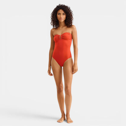 Model wearing Shop Rescue Spa Cassiopee Rooibos red one-piece bustier swimsuit with front shirring and U-shaped link.