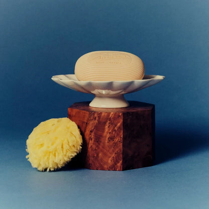Shop Rescue Spa Bienaimé shell-shaped ceramic soap dish with a creamy glaze and scalloped rim on a wooden pedestal