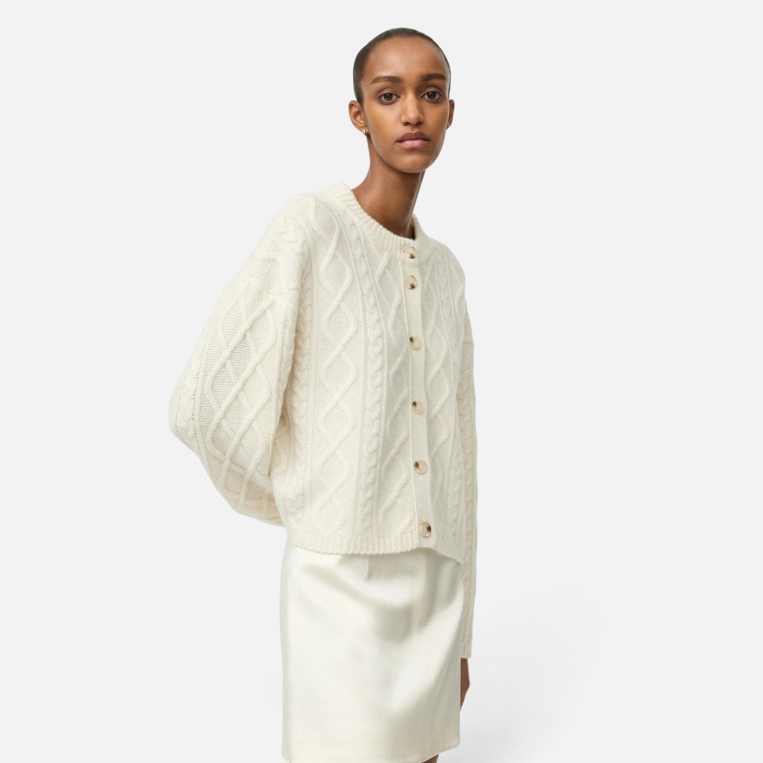 Shop Rescue Spa cream cable knit cashmere cardigan with button front, worn by a model against a neutral background.