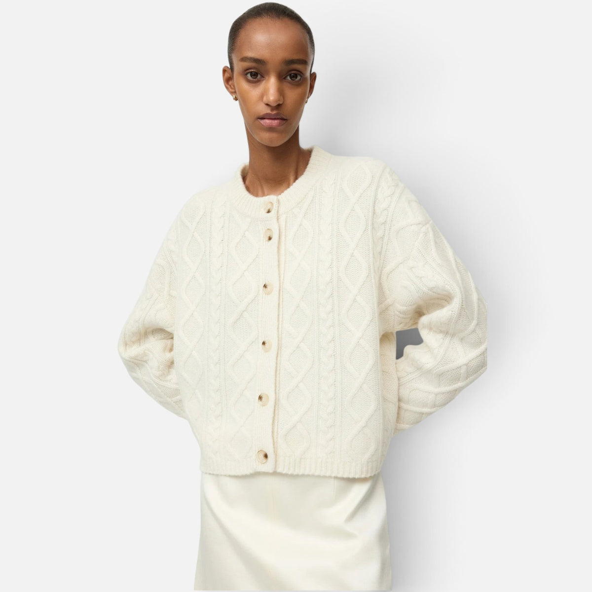 Shop Rescue Spa cream cable knit cashmere cardigan with button-up front worn by a model against a white background