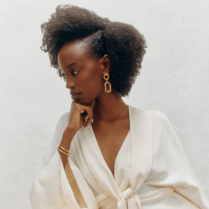 Shop Rescue Spa woman with defined natural curls wearing a white robe and gold jewelry, showcasing hair product.