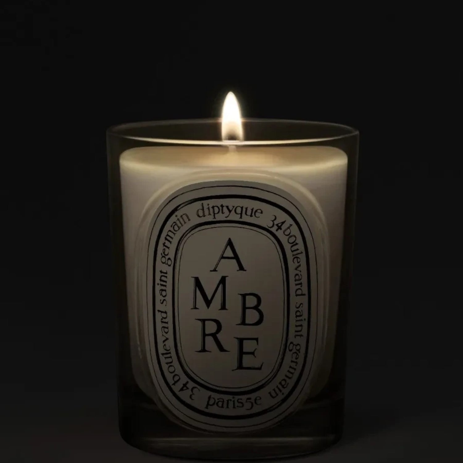 Shop Rescue Spa Diptyque Ambre scented candle in a glass vessel with a glowing flame against a dark background