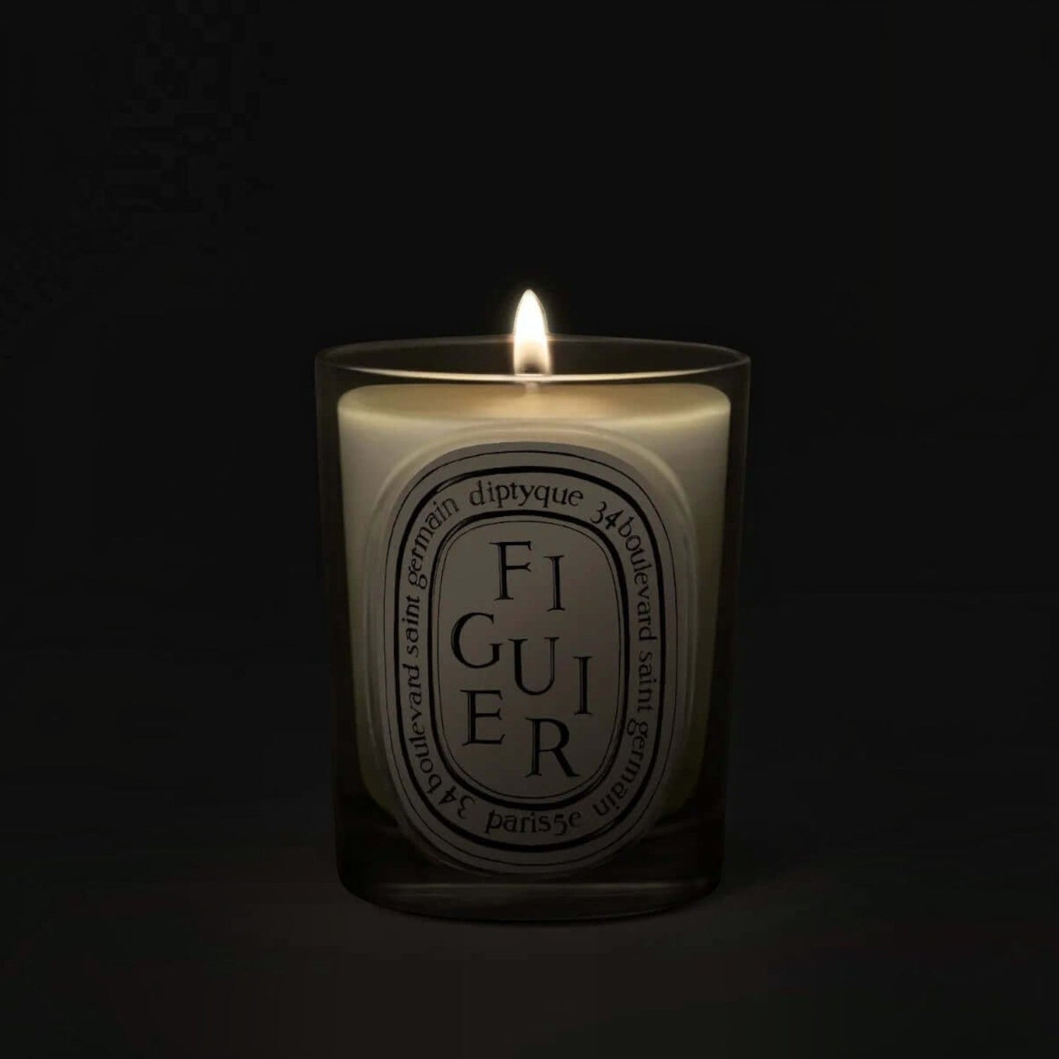 Shop Rescue Spa Diptyque Figuier candle in a clear glass vessel with a glowing flame against a dark background