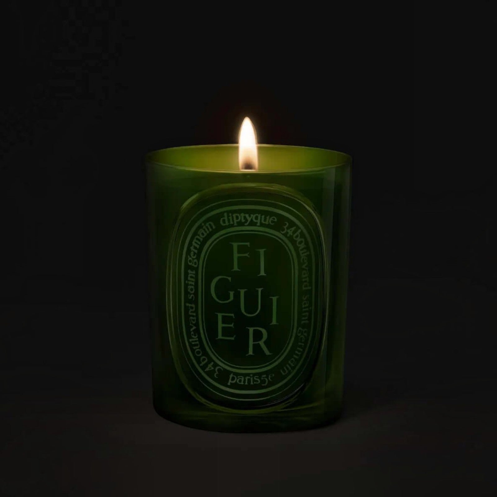 Shop Rescue Spa Diptyque Figuier candle in a green glass vessel with a glowing flame against a dark background