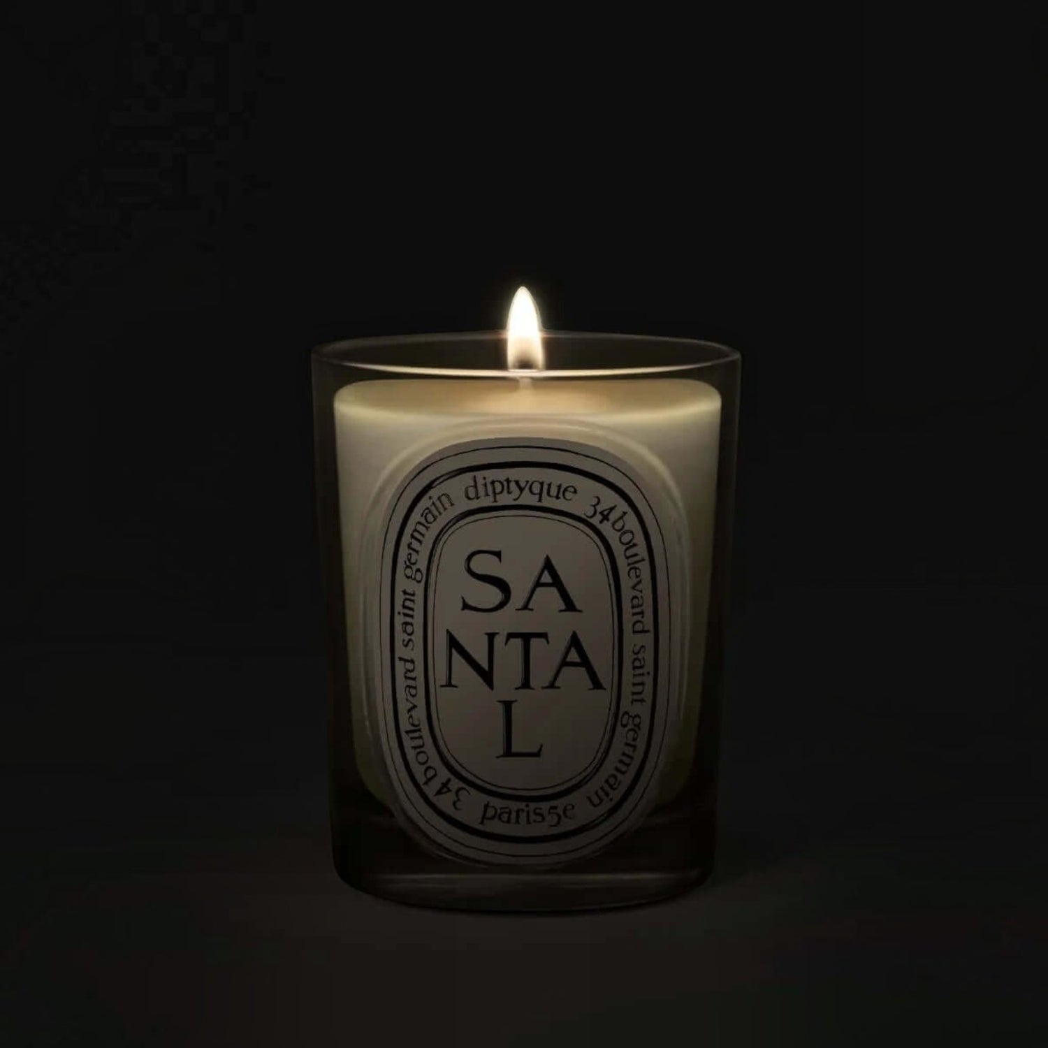 Shop Rescue Spa Diptyque Santal scented candle in a glass vessel with a glowing flame against a dark background