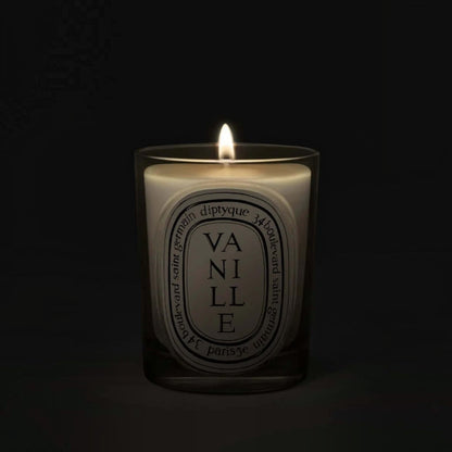 Shop Rescue Spa Diptyque Vanille scented candle in a glass vessel with a glowing flame against a dark background.