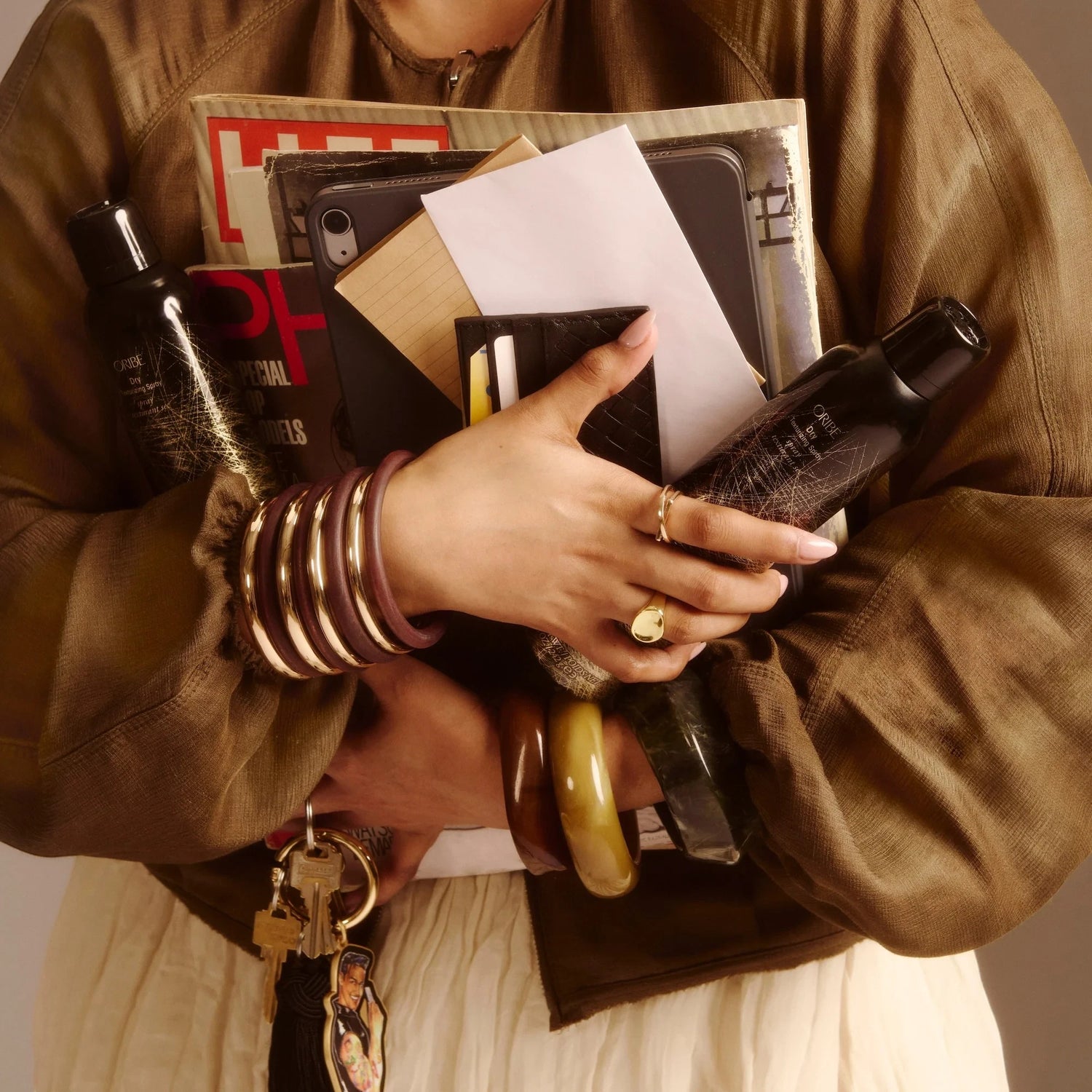 Shop Rescue Spa Dry Texturizing Spray bottles held by a person carrying magazines, a tablet, and a wallet.