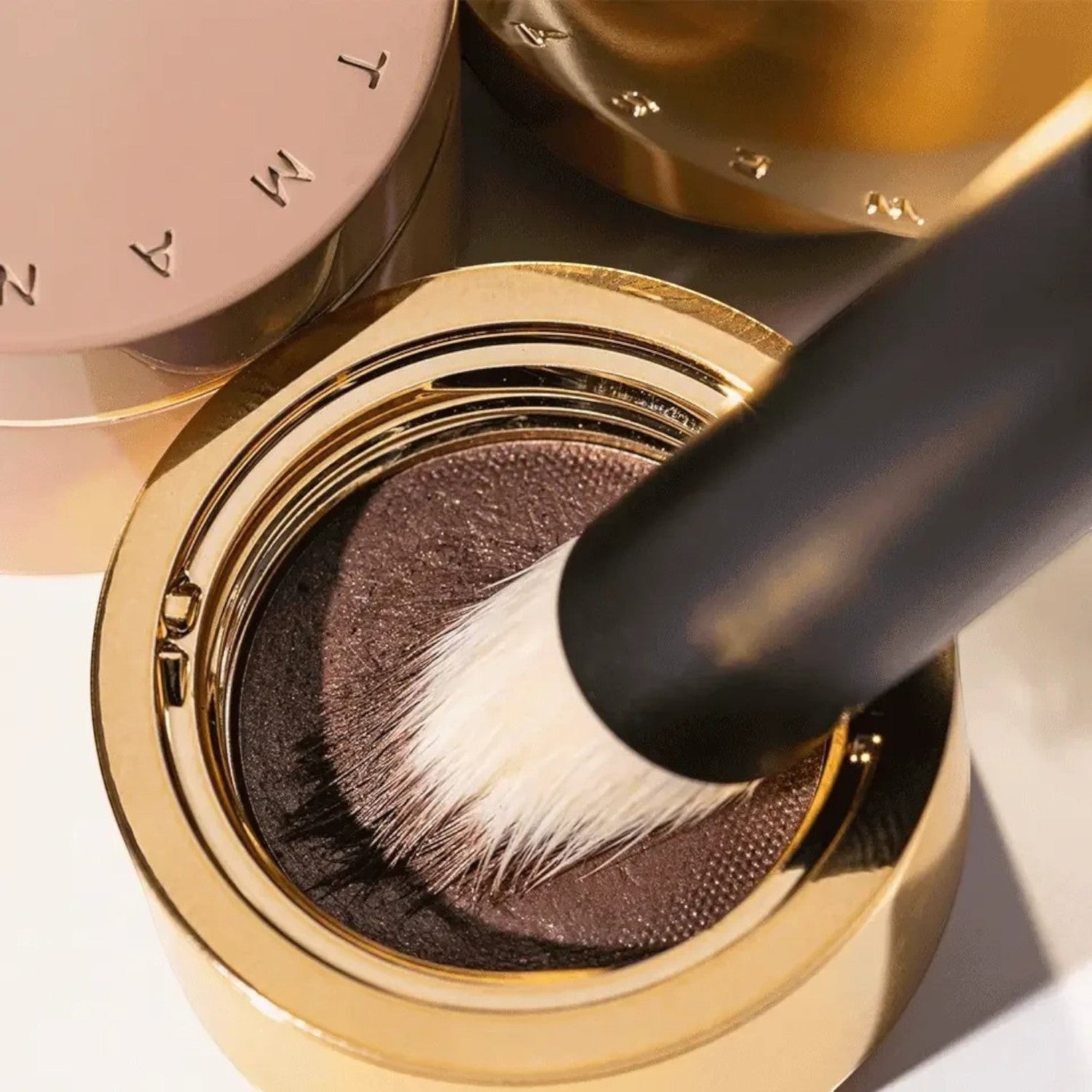 Shop Rescue Spa Eye Shadow Brush II with soft white nylon bristles picking up dark brown powder from a gold compact