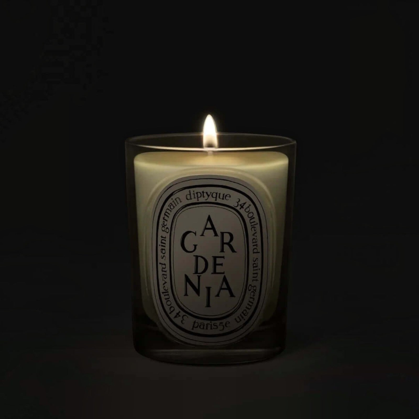 Shop Rescue Spa Gardenia scented candle in a glass vessel with a lit wick glowing against a dark background