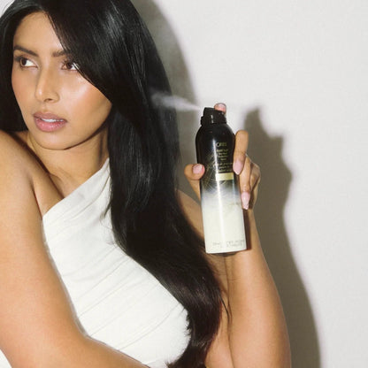 Shop Rescue Spa model with long dark hair spraying Oribe Gold Lust Dry Heat Protection Spray, protecting hair from heat.