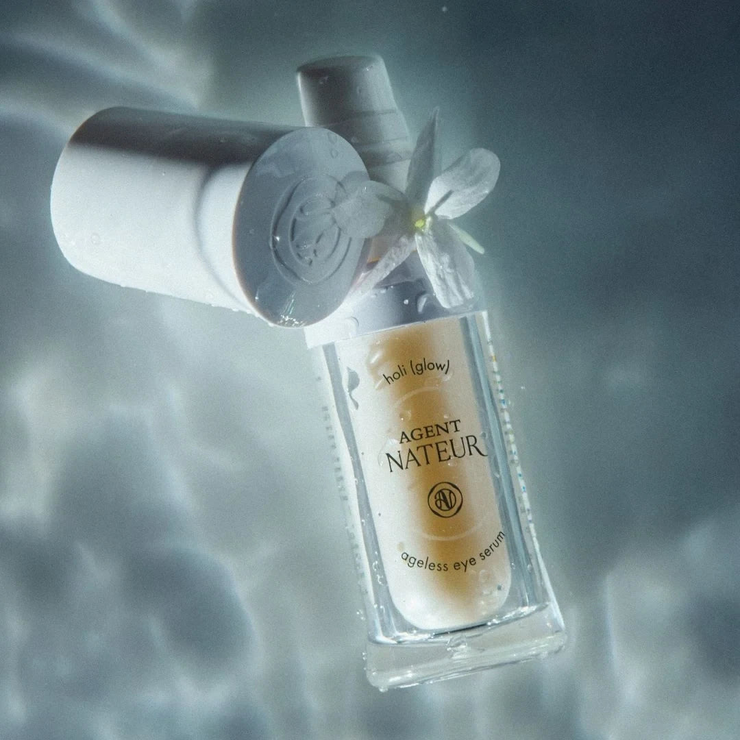 Shop Rescue Spa Holi (glow) Ageless Eye Serum in a clear glass bottle with white cap, floating in water with a flower.