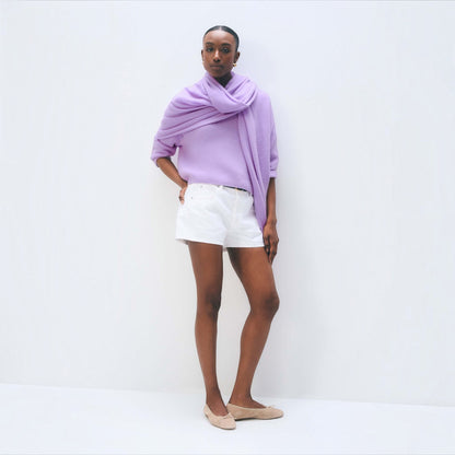 Model wearing a Shop Rescue Spa lavender fog cashmere travel wrap as a scarf over a light purple sweater and shorts.