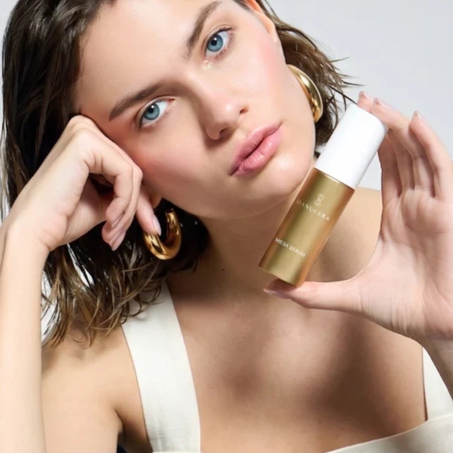 Shop Rescue Spa Mega Serum held by a model with glowing skin, featuring a gold bottle with a white cap.
