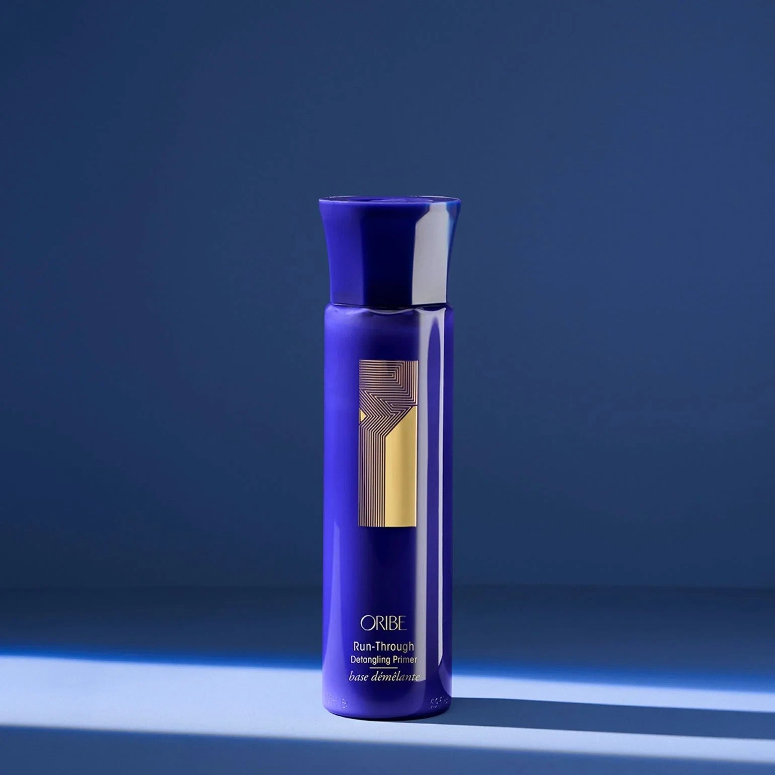Shop Rescue Spa Oribe Run-Through Detangling Primer in a deep blue bottle with gold accents on a blue background.