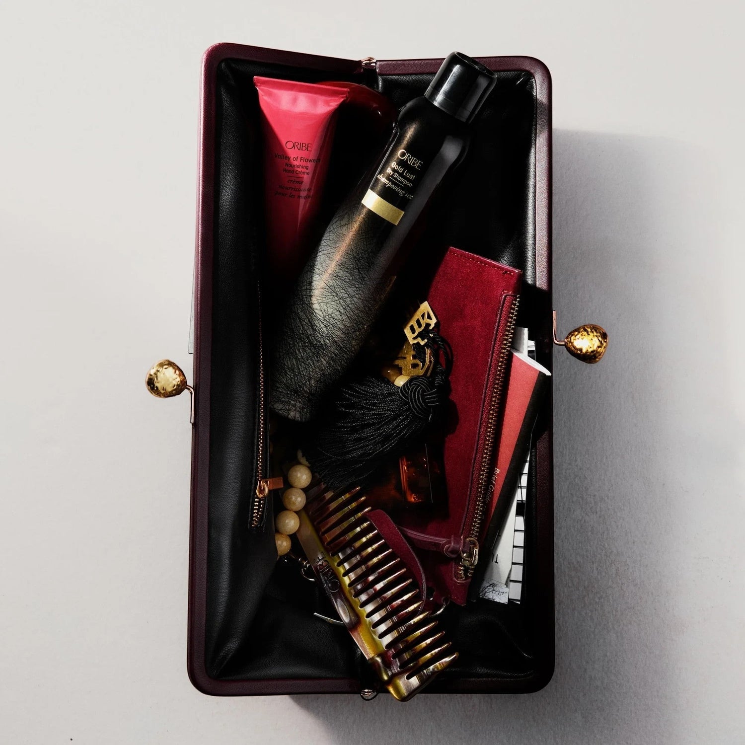 Shop Rescue Spa Oribe Gold Lust dry shampoo inside a dark burgundy clutch with a comb and beauty products