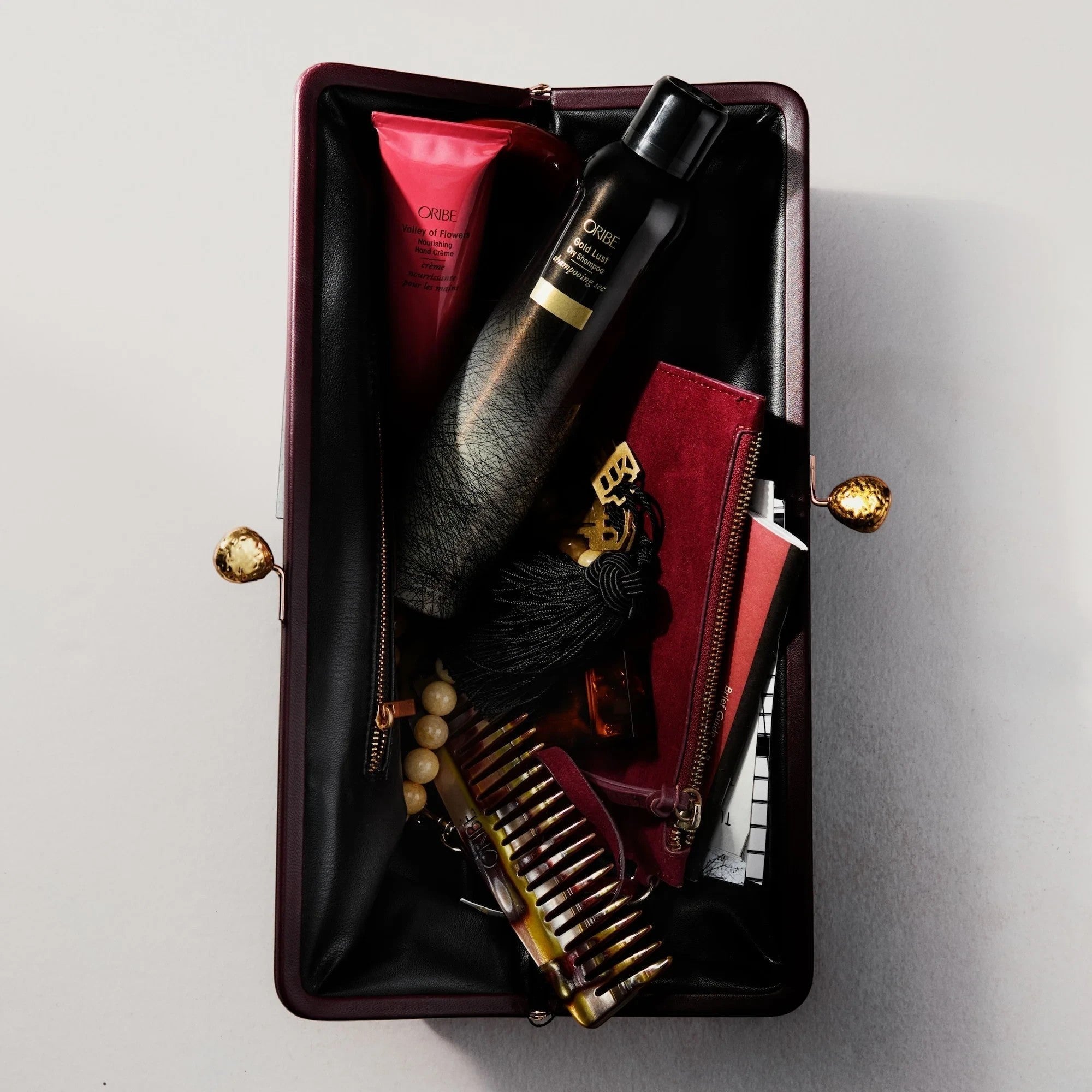 Shop Rescue Spa Oribe Gold Lust dry shampoo inside a dark burgundy clutch with a comb and beauty products