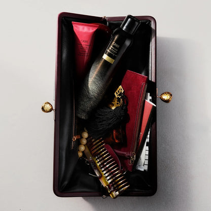 Shop Rescue Spa Oribe Gold Lust dry shampoo inside a dark burgundy clutch with a comb and beauty products
