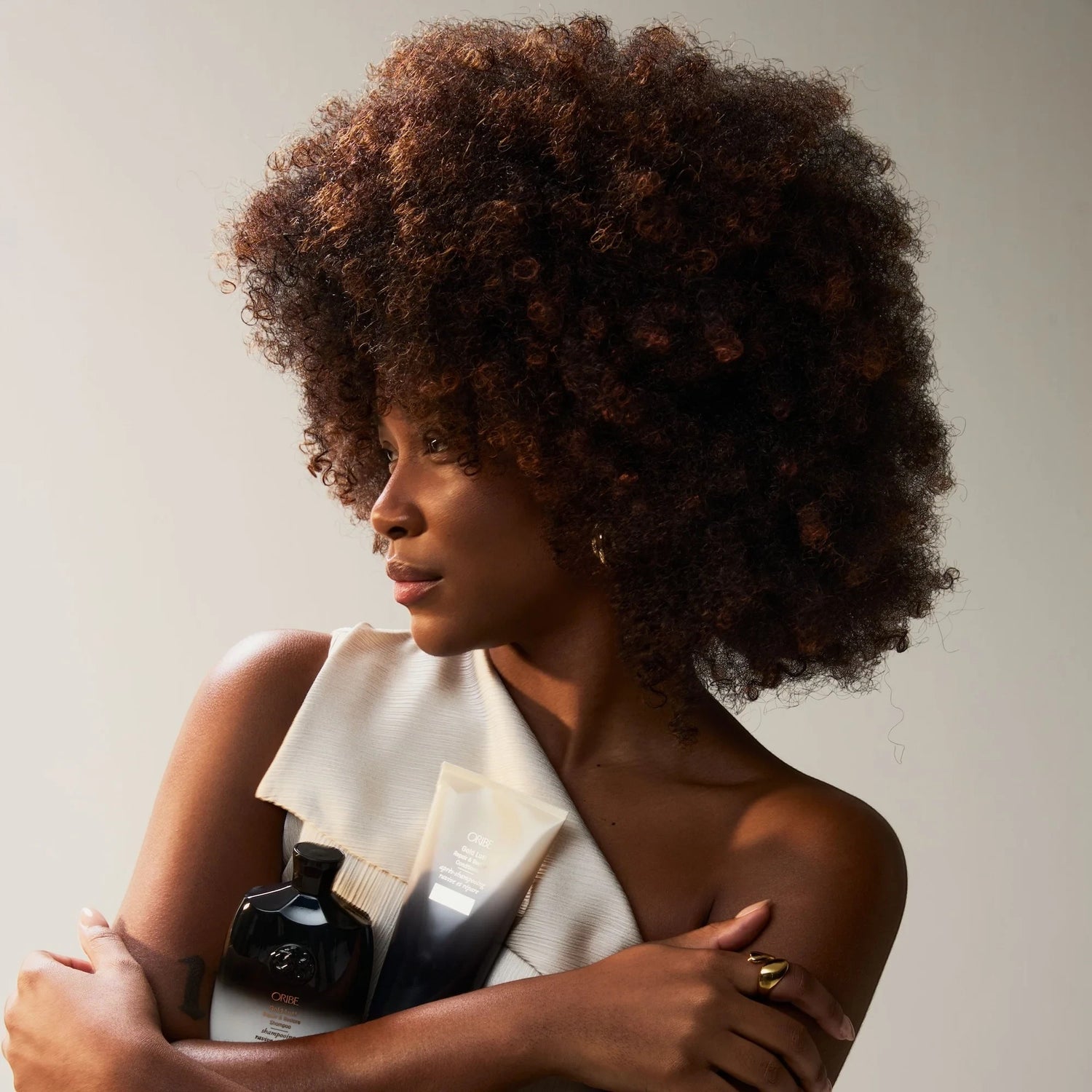 Shop Rescue Spa model with voluminous curly hair holding Oribe Gold Lust Repair and Restore shampoo and conditioner