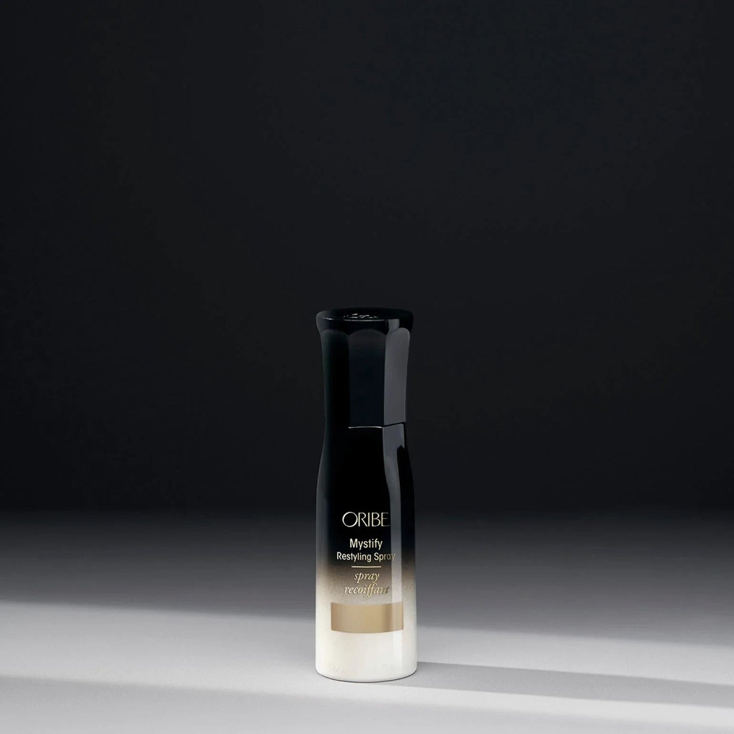 Oribe Mystify Restyling Spray bottle with gold and white gradient, provides heat protection and strengthens hair.