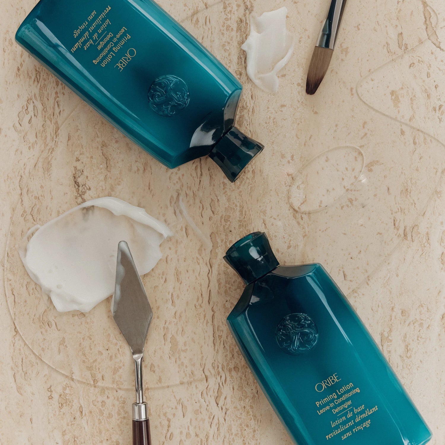 Shop Rescue Spa Oribe Priming Lotion Leave-In Conditioning Detangler in teal bottles, with dollops of white cream and clear gel.