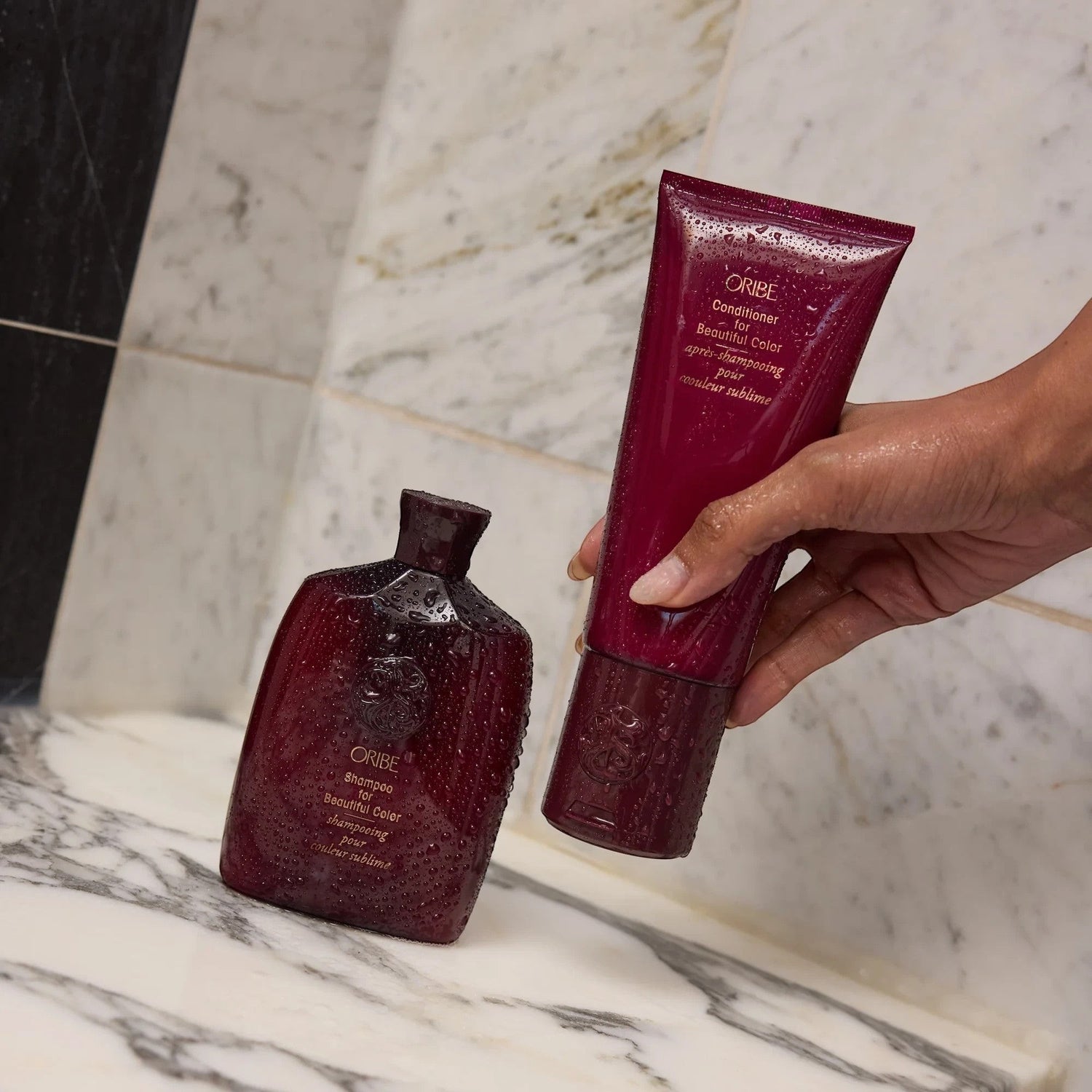 Shop Rescue Spa Oribe Shampoo and Conditioner for Beautiful Color bottles with water droplets on a marble surface