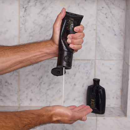 Shop Rescue Spa Oribe Signature Conditioner being squeezed from a black tube into a hand in a marble shower
