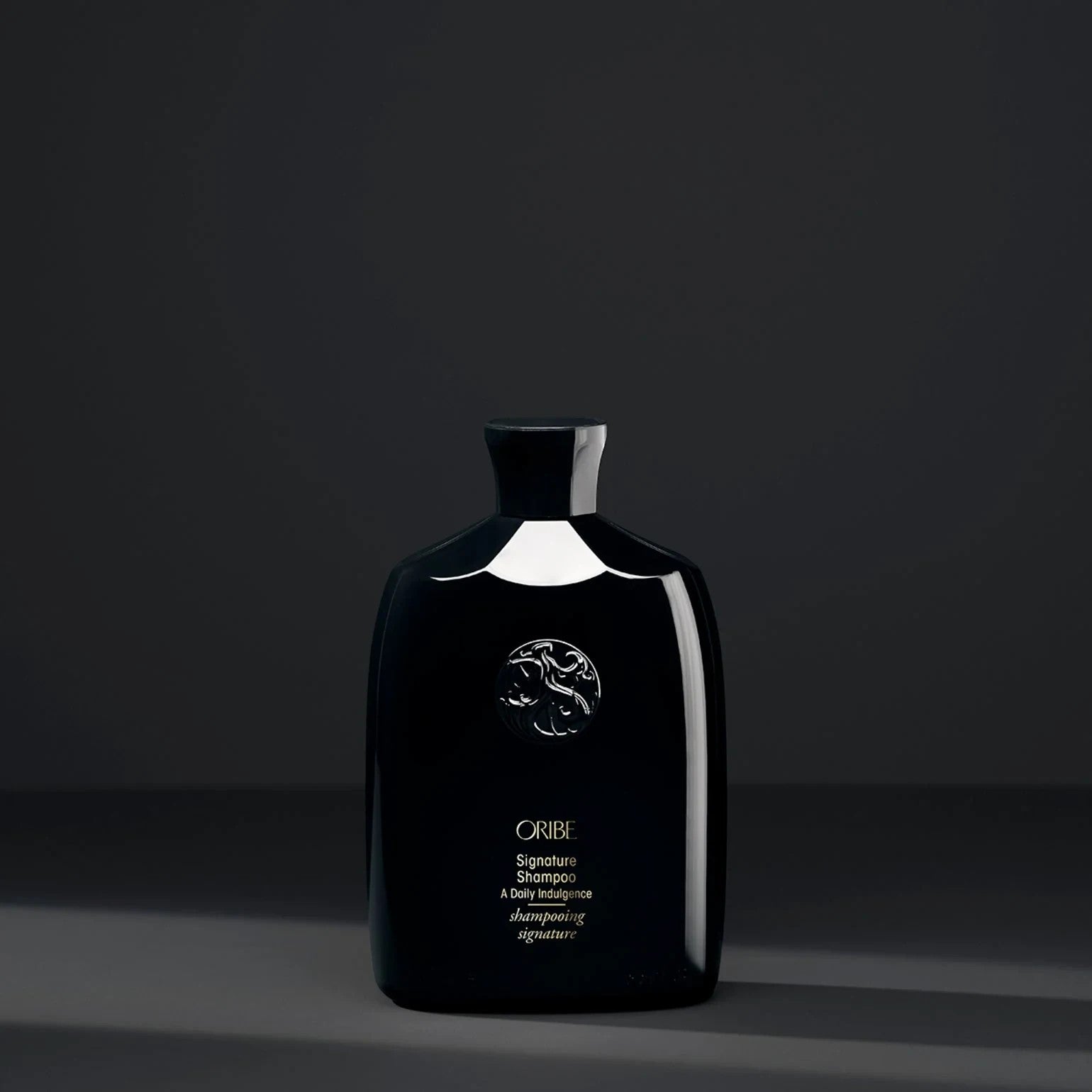 Shop Rescue Spa Oribe Signature Shampoo in a sleek black bottle with gold lettering against a dark grey background.