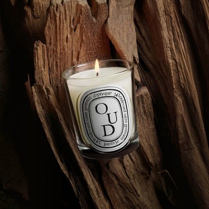 Shop Rescue Spa Oud scented candle in a glass vessel with a lit wick, set against a rustic textured wood background.