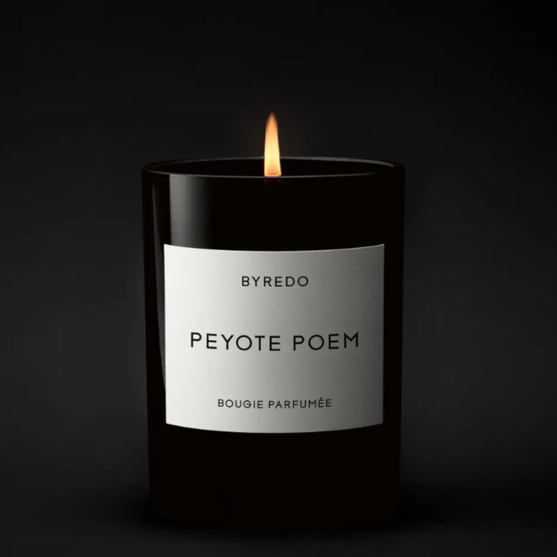 Shop Rescue Spa Byredo Peyote Poem candle in a black glass vessel with a white label. Lit candle with a flame.