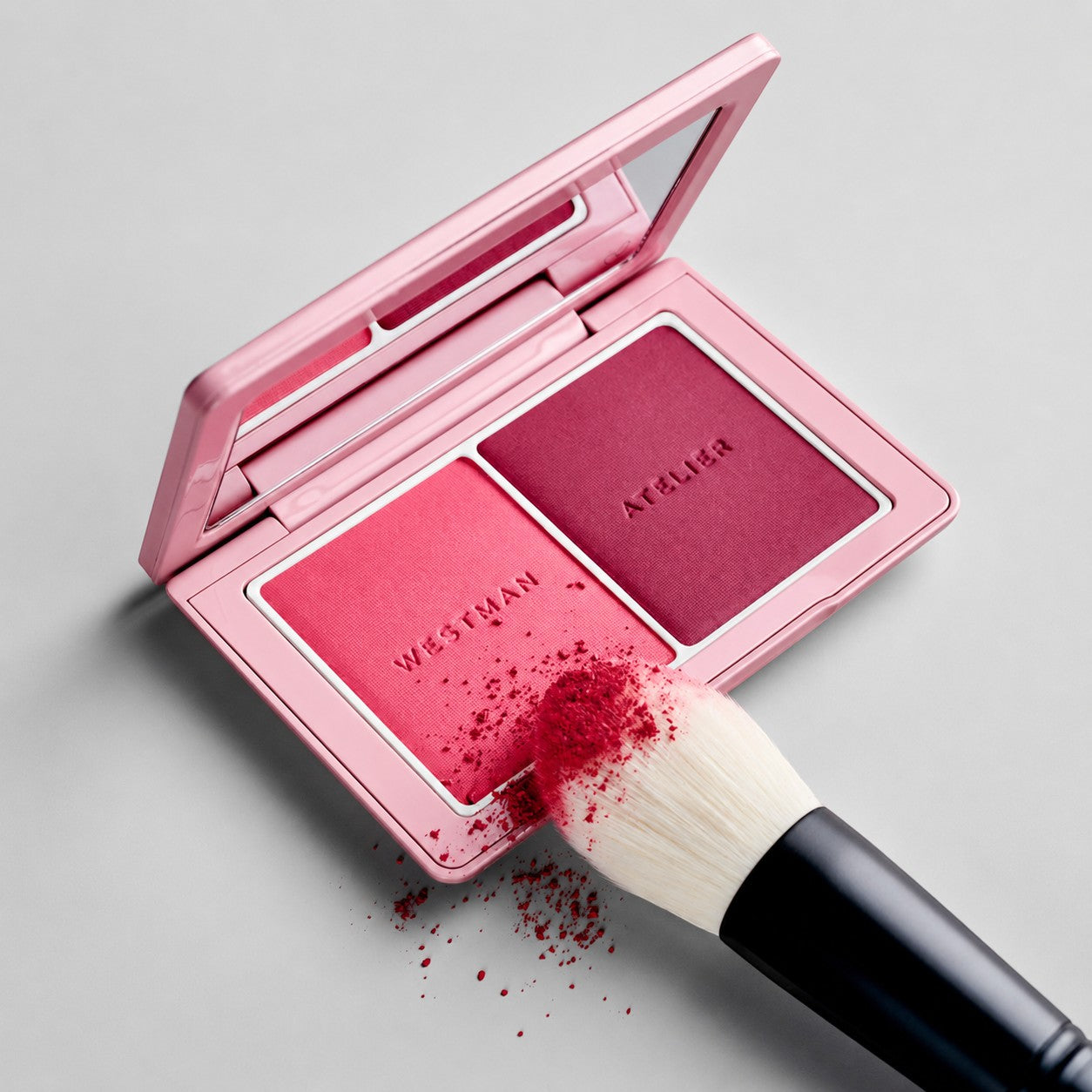 Shop Rescue Spa Powder II brush with soft bristles picking up pink and berry powder blush from a Westman Atelier palette