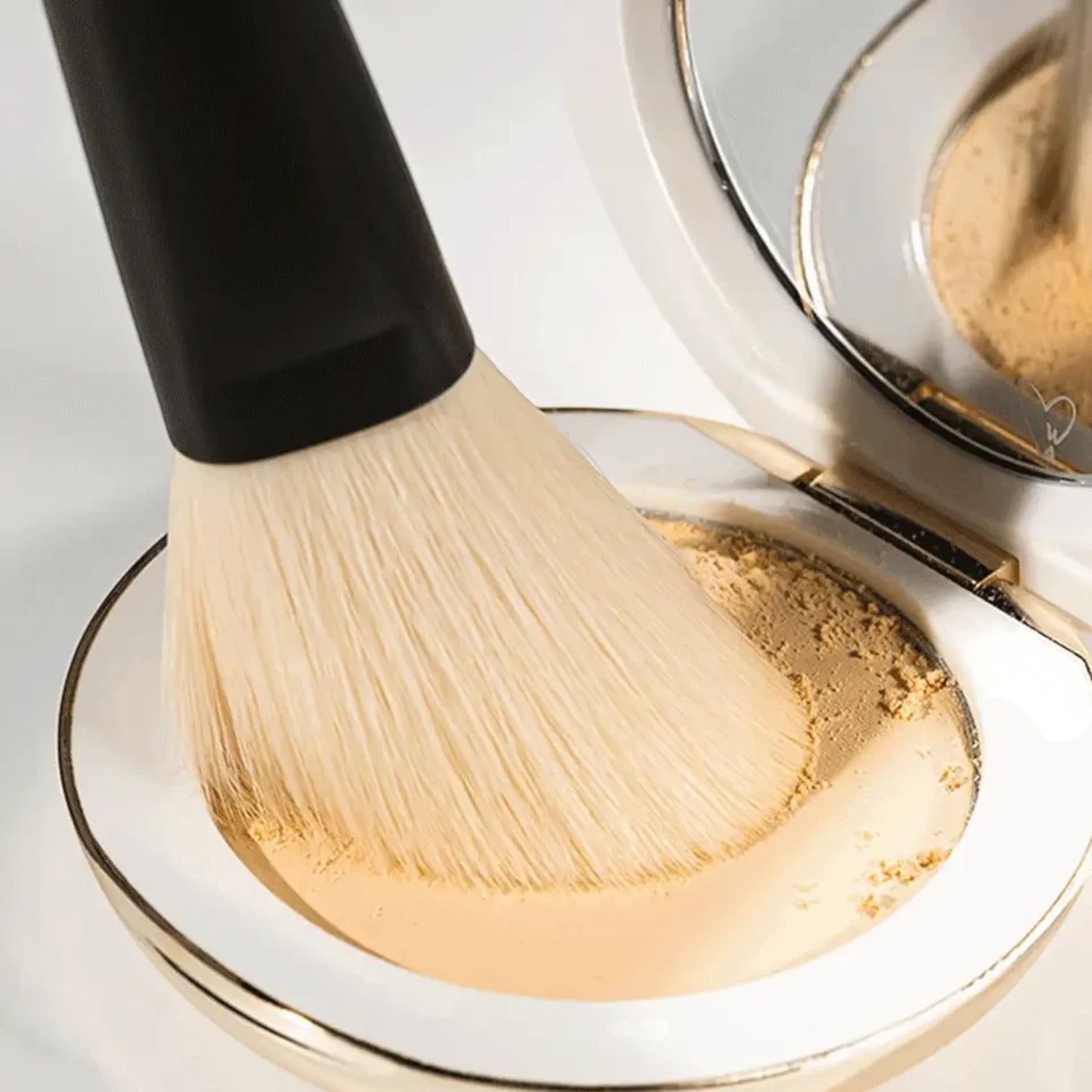 Shop Rescue Spa powder brush with soft nylon bristles picking up bronzer from a compact mirror case