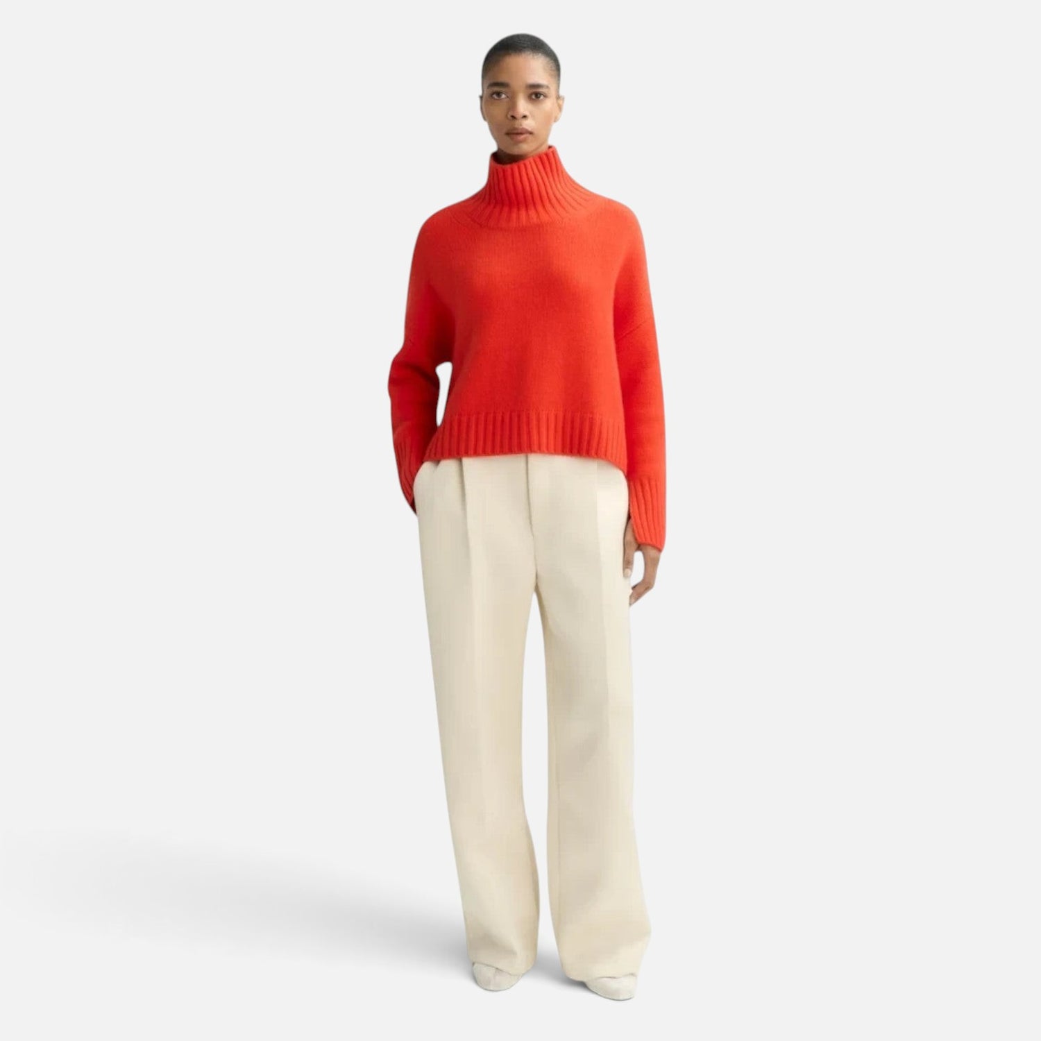 Model wearing a Shop Rescue Spa chunky red cashmere turtleneck sweater with sleeve slits and cream wide-leg trousers.