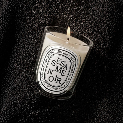 Shop Rescue Spa Sesame Noir scented candle in a glass vessel, surrounded by a bed of roasted black sesame seeds.