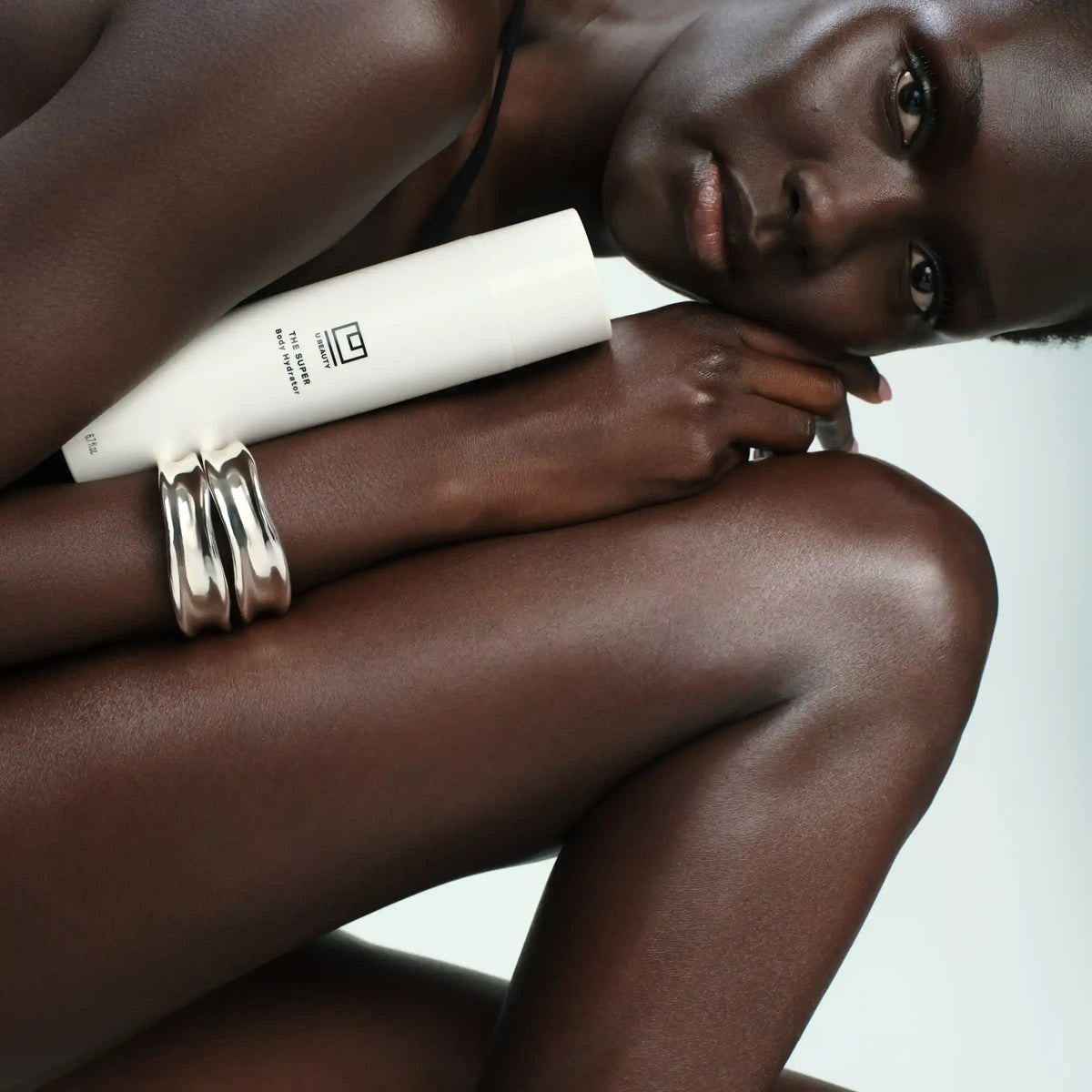 Shop Rescue Spa The Super Body Hydrator white tube held by a model with radiant skin and silver bracelets