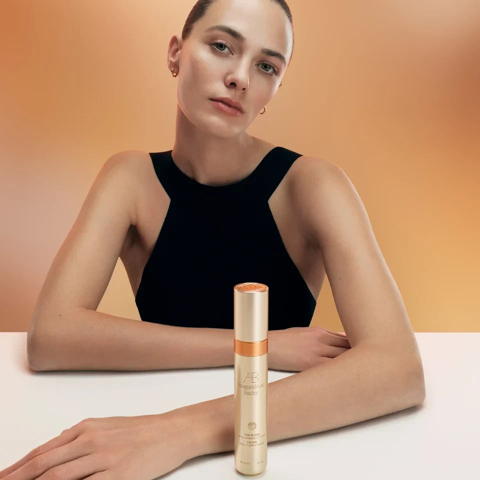 Shop Rescue Spa The Elixir anti-aging serum in a gold bottle with a model posing in a black top against a warm background