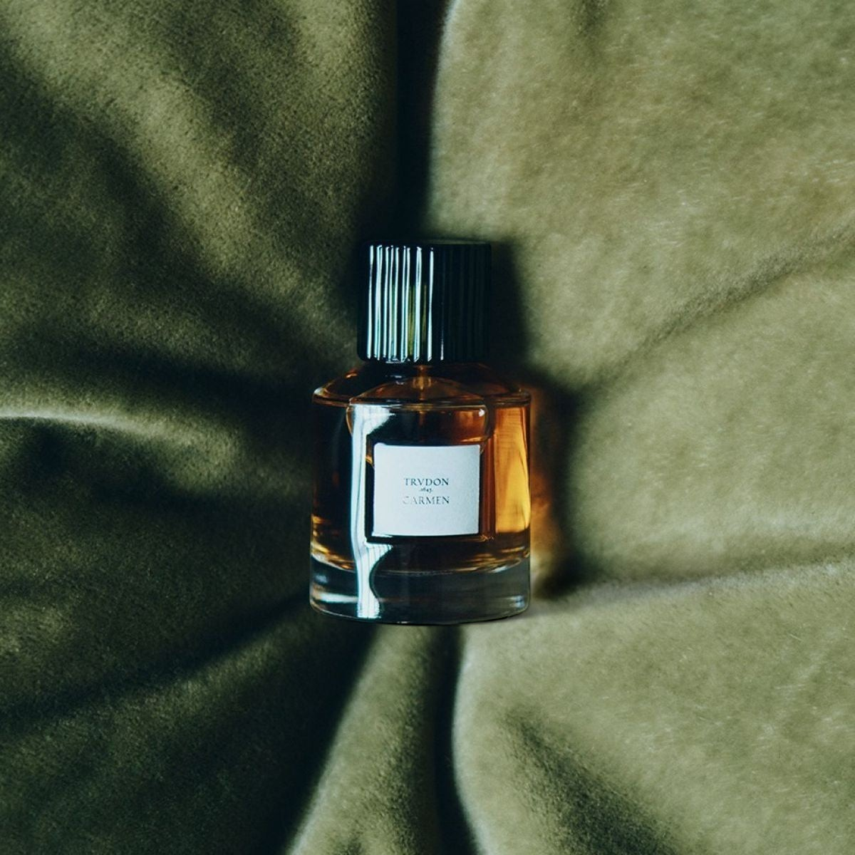 Shop Rescue Spa Trudon Carmen Eau de Parfum in a glass bottle with a black cap resting on soft olive green velvet.