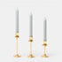 Trudon gold-plated candlestick trio with Madeleine taper candles, arranged smallest to tallest on a grey background